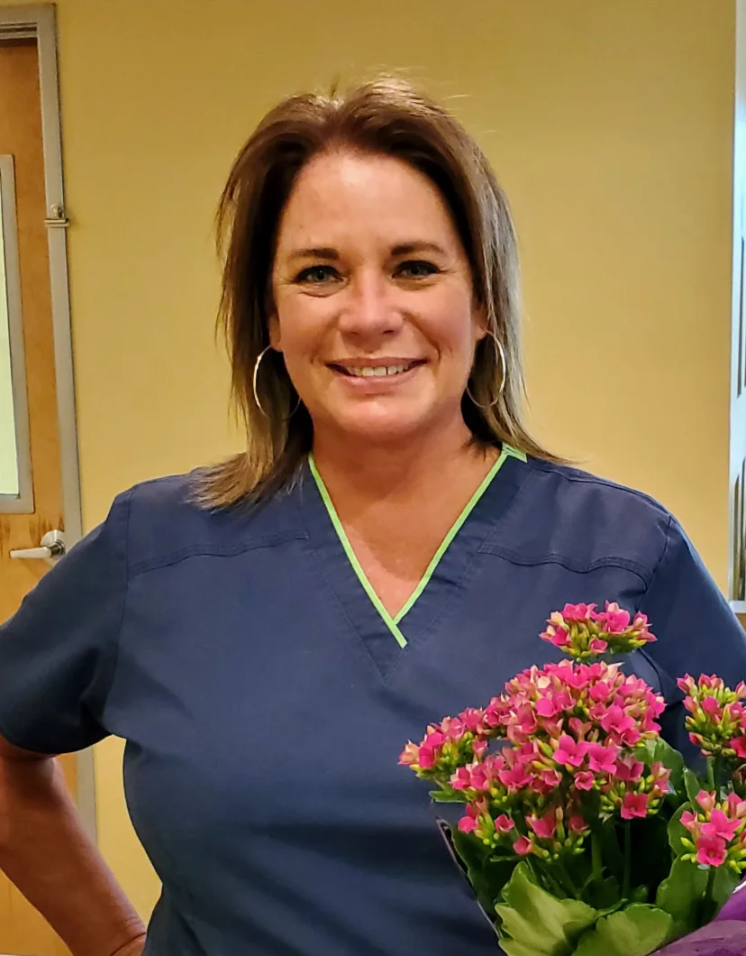 Cara Longshore smiling inside next to a bouquet of pink flowers.